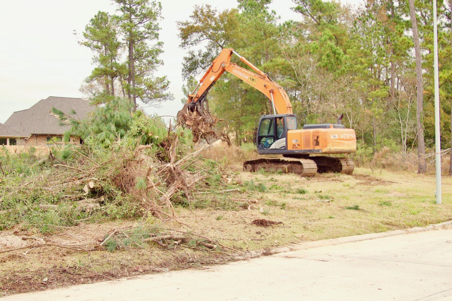 An excavator lifting brush and root balls off a residential lot in the Houston area