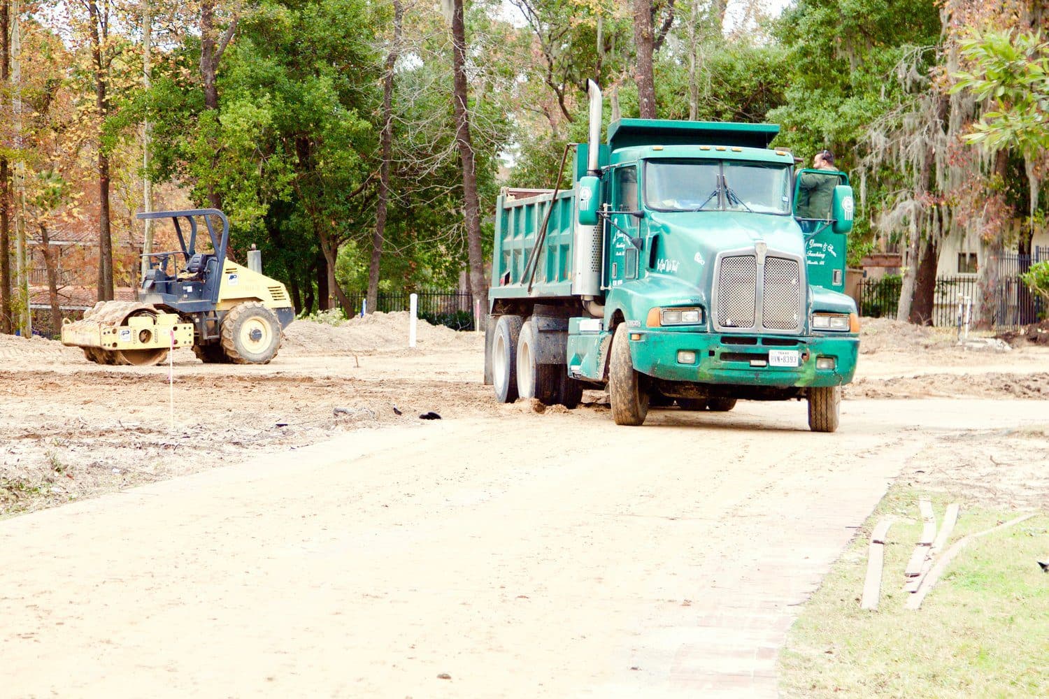 A dump truck and a roller working a building pad on a Houston-area lot